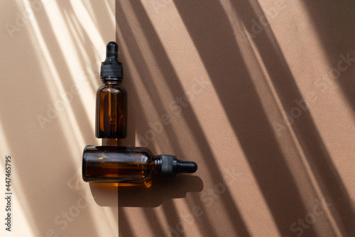 Mock-Up of two glass dropper bottles on abstract two-color background in rays of sunlight. Shadows in form of stripes fall on beige-brown surface. Concept of body care