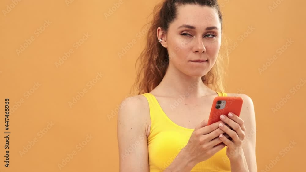 A thinking woman wearing yellow sport suit using her mobile isolated over yellow background A thinking woman wearing yellow sport suit using her mobile isolated over yellow background