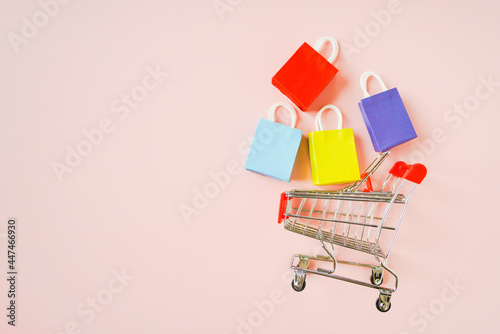 side of shopping cart and small multi colored shopping bags on pink background