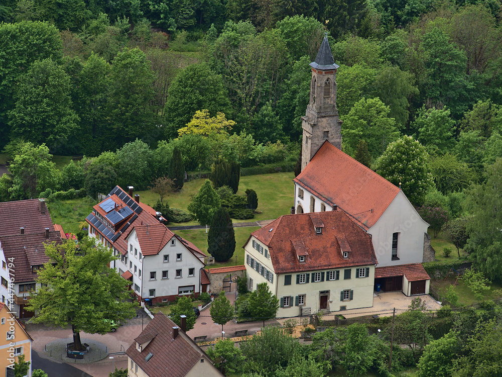 Aerial view of idyllic village Honau, part of Lichtenstein, Germany located in Echaz valley in Swabian Alb with historic church Galluskirche surrounded by green trees in spring season.