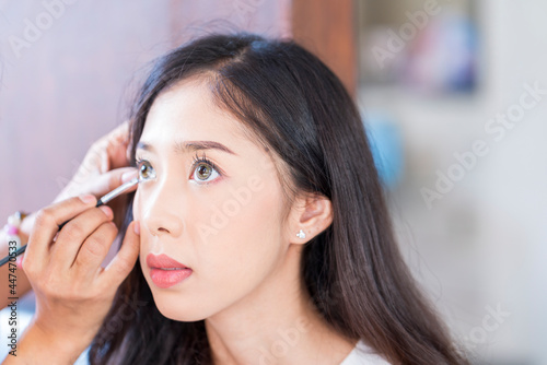 Young beautiful woman with Makeup Brush. Two friends making up in the cafe. Asian girl. Friends are mascara brush.