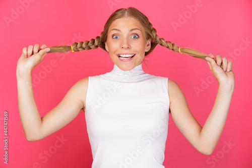 Portrait of cute smiling and fool around woman holding long hair pigtails on red background.