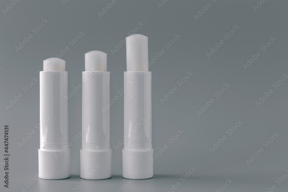 Side view of white lip balm tubes on gray background. Side view of white lip balm tubes on gray background.