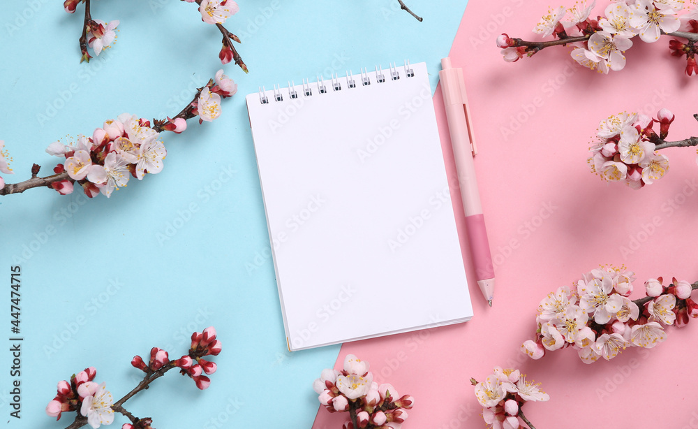 Notebook and beautiful flowering branches on pink blue background. Flat lay, top view.