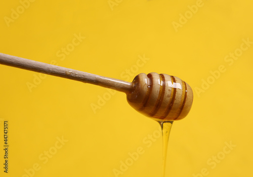 Honey bee spoon with liquid honey on yellow background.