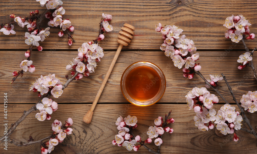 Honey Bee jar with wooden spoon and beautiful flowering branch on wooden background. Springtime concept