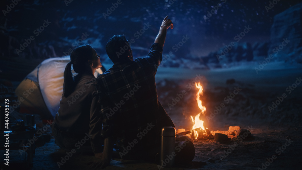 Fototapeta premium Happy Couple Nature Camping in the Canyon, Sitting by Campfire Watching Night Sky with Milky Way Full of Bright Stars. Two Travelers In Love On a Romantic Vacation Trip. Back View Shot