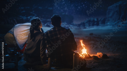 Happy Couple Tent Camping in the Canyon  Sitting by Campfire Watching Night Sky with Milky Way Full of Bright Stars. Two Travelers In Love On a Romantic Vacation Trip. Back View Shot