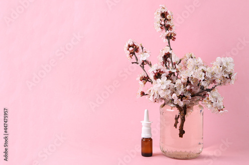 Nasal spray and Beautiful flowering branches in glass jar on pink background.