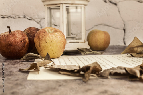 Autumn background, composition of wrinkled apples, next to poem, lantern and dry autumn leaves.