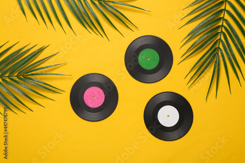 Vinyl records and palm green leaves on yellow background. Music concept. Tropical composition. Top view. Flat lay