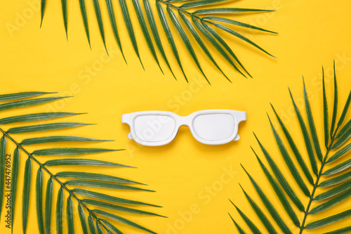 White sunglasses and palm leaves on yellow background. Tropical, minimal layout. Top view. Flat lay