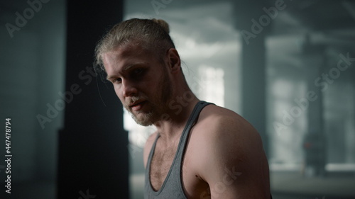 Athlete posing at camera in gym. Athletic man sitting on rubber tire with hammer