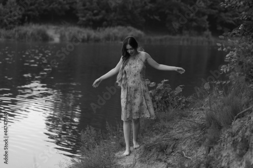 Young long haired woman in dress standing near the lake in black and white