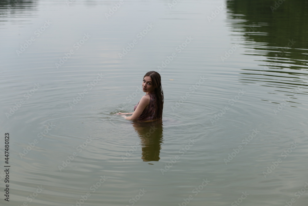 Fototapeta premium Long haired woman in pink dress swimming in the lake