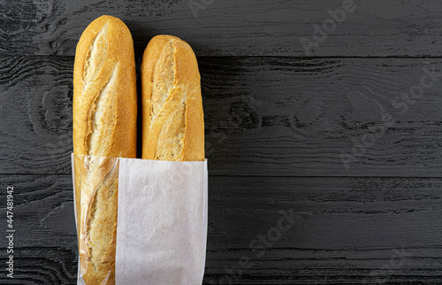 French bread mini baguette in a paper bag on a black wooden table. Top view, copy of the space