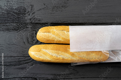 French bread mini baguette on an old black, dark wooden table in a white paper bag. Rustic style.Top view, copy of the space
