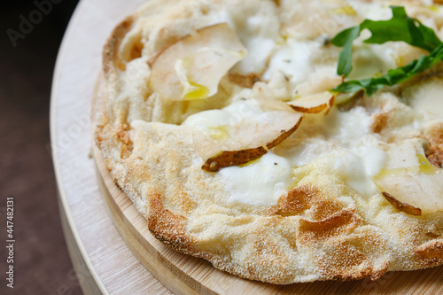 Roman round pizza five or four cheeses with baked pear on a round wooden kitchen pizza board. Delicious fresh Italian pizza on a round wooden table. Shallow depth of field