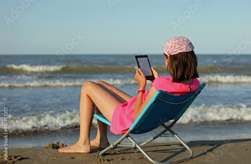 girls arrives on the sea beach reads an e-book and has the bandana on her head