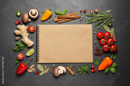 Open recipe book and different ingredients on black table, flat lay. Space for text photo