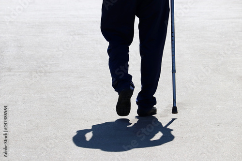 Silhouette of man walking with a cane down the street, shadow on asphalt. Concept of old age, diseases of the spine or joint disease, elderly people