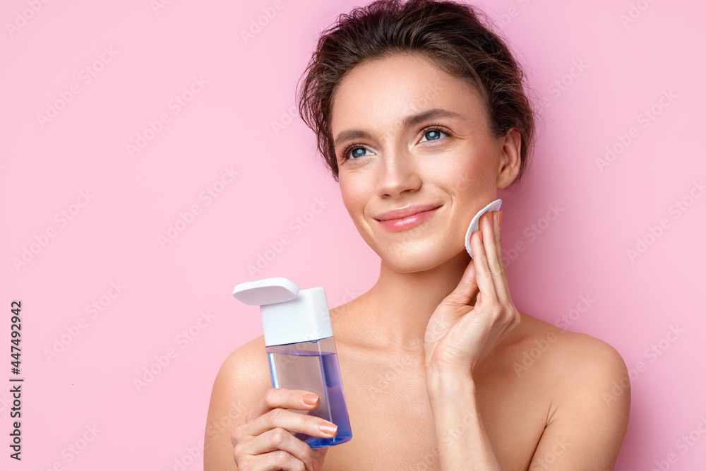 Woman removing makeup, holds cotton pads near face. Photo of woman with perfect skin on pink background. Beauty and skin care concept Woman removing makeup, holds cotton pads near face. Photo of woman with perfect skin on pink background. Beauty and skin care concept
