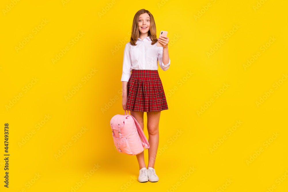 Full size photo of cute small girl hold telephone wear shirt skirt bag sneakers isolated on yellow background Full size photo of cute small girl hold telephone wear shirt skirt bag sneakers isolated on yellow background