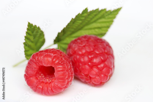 Ripe raspberries with green leaves on white background. Red juicy berries close up, summer crop