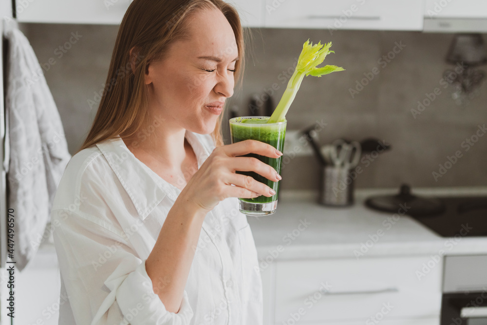 Young woman drinking healthy spinach and celery smoothie at home in the kitchen Young woman drinking healthy spinach and celery smoothie at home in the kitchen