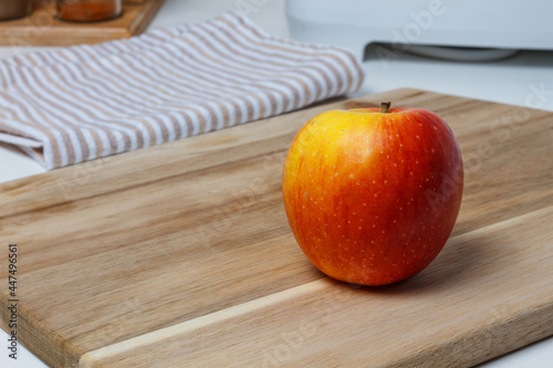 A red apple on the kitchen chopping board. A black ceramic knife and a towel.