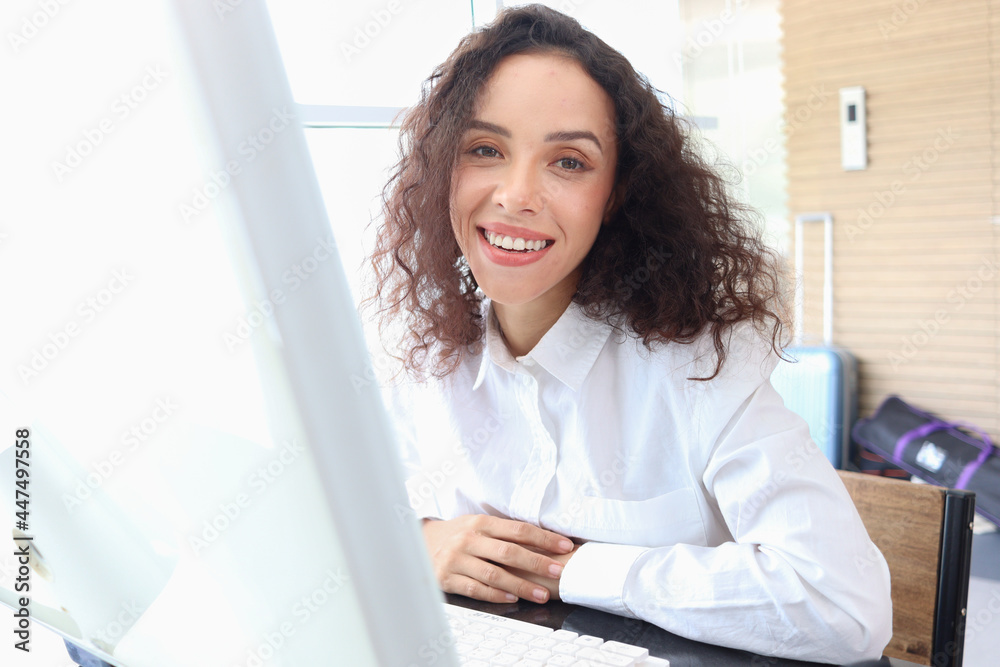 Portrait of happy smiling young beautiful woman with curly hair using desktop computer, female officer staff in casual white shirt sitting at working desk at office workplace. Portrait of happy smiling young beautiful woman with curly hair using desktop computer, female officer staff in casual white shirt sitting at working desk at office workplace.