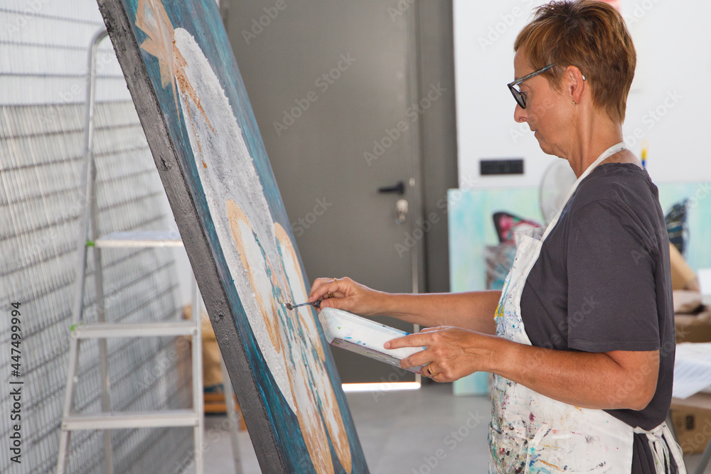 Detail of a mature woman painting a butterfly on a white canvas in her studio. Concept art and artist.