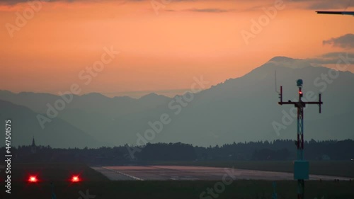 Business jet landing against dramatic and colorful sunset. Airplane descending. Long runway, Ljubljana airport, Slovenia. View of Alps in the distance. Private jet touchdown. Static shot