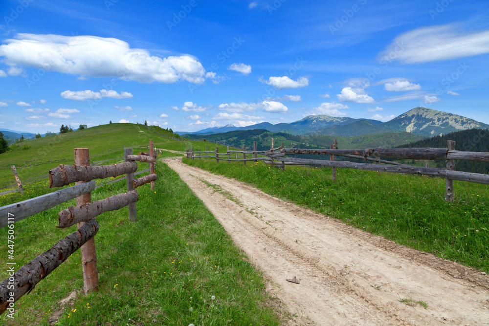 Mountain road with a wooden fence, bright blue sky. Ukraine, Carpathians.