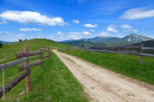 Mountain road with a wooden fence  bright blue sky. Ukraine  Carpathians.