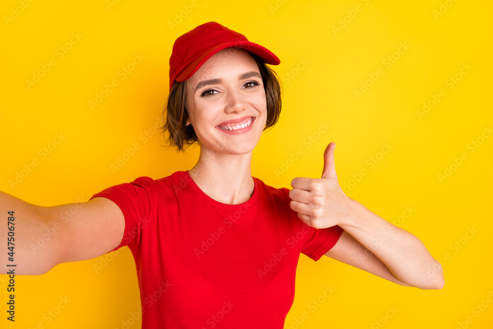 Photo portrait of woman in red uniform cap taking selfie smiling showing thumb-up sign isolated on bright yellow color background