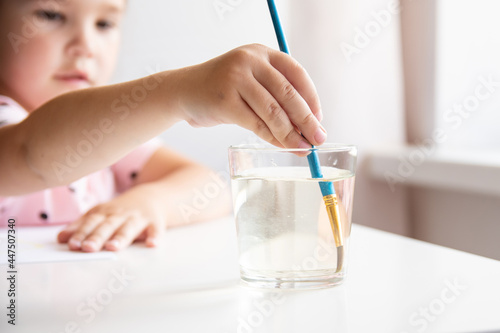 The child's hand holds a brush in a glass of water. The concept is a small child drawing.