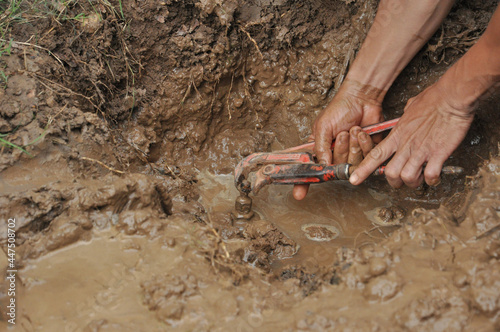 hands fix leaking plumbing with pliers in the mud