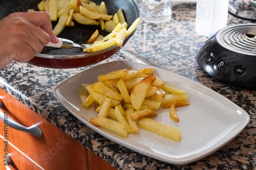 French fries being served from a pan to a dish