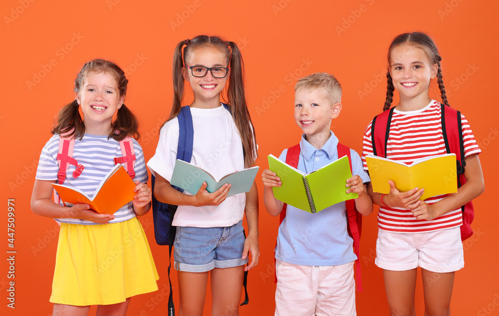 Group of happy pupils with exercise books standing next to orange background Group of happy pupils with exercise books standing next to orange background