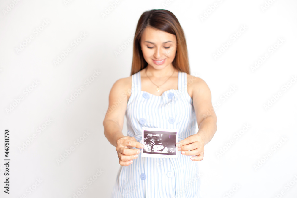 A young beautiful pregnant woman shows a picture of the ultrasound and looks at her tummy with love. Care and tenderness. White background. Screening in pregnancy. White background, space for text A young beautiful pregnant woman shows a picture of the ultrasound and looks at her tummy with love. Care and tenderness. White background. Screening in pregnancy. White background, space for text