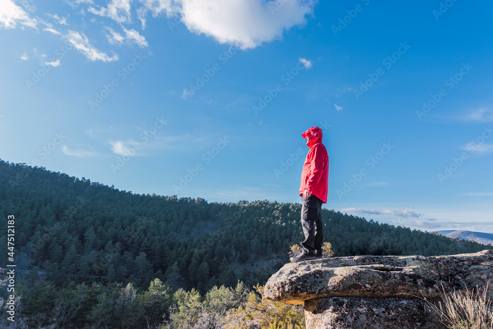 Naklejka premium man on a rock dressed in red, looking at the landscape around him