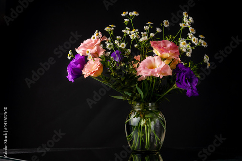 Bouquet of eustoma with boxwood and small-leaved branches on a table on a black background