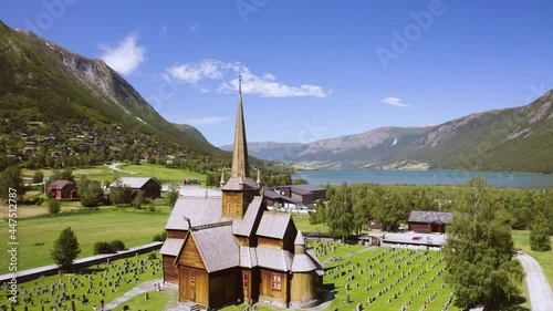 Wooden Church And Cemetery Under The Sunlight. Lom Stave Church With Otta River In Lom, Norway. aerial orbit photo