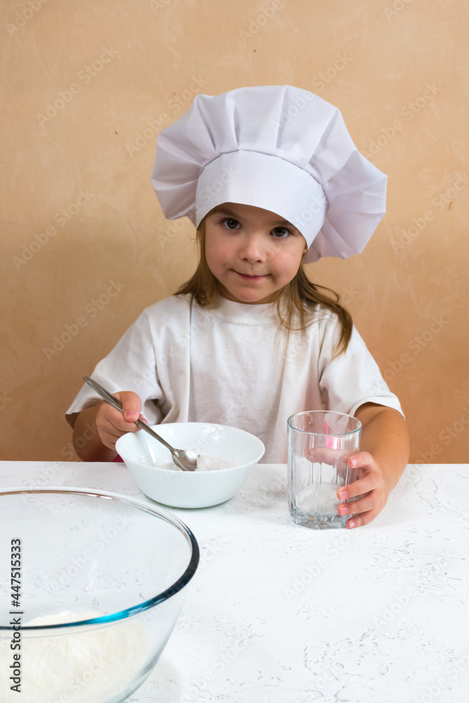 A little girl dressed as a cook kneads the dough. Cooking child lifestyle concept. The kid loves, has fun, studies and plays in the kitchen A little girl dressed as a cook kneads the dough. Cooking child lifestyle concept. The kid loves, has fun, studies and plays in the kitchen