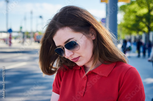 A woman in red polo and sunglasses is looking down on the street