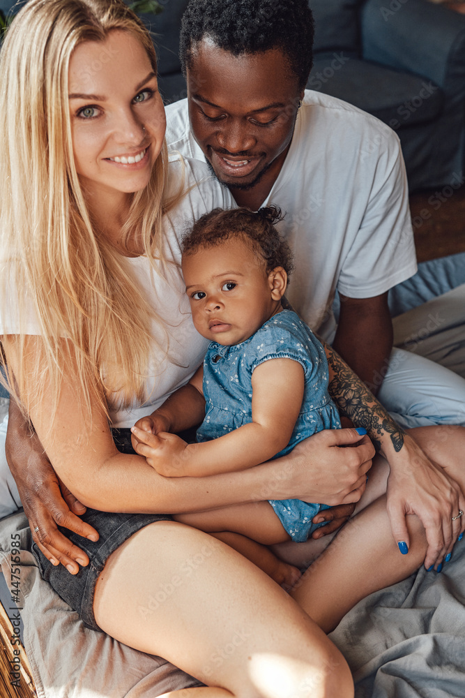 Cheerful little girl with her multiethnic parents on bed