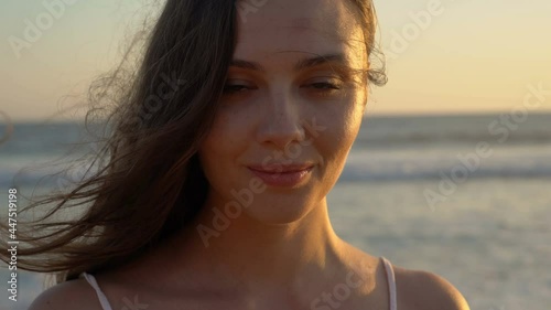 Portrait of a young dark-haired woman with freckles on the background of the sea at sunset.