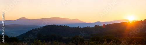 Beautiful mountain panorama of landscape with hazy peaks and foggy wooded valley at sunset.