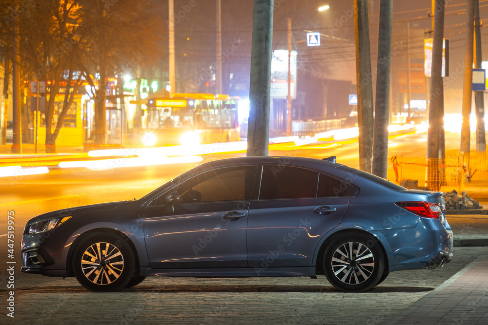 Obraz premium Close up of parked car on roadside at night with blurred view of traffic lights of moving vehicles on city street.